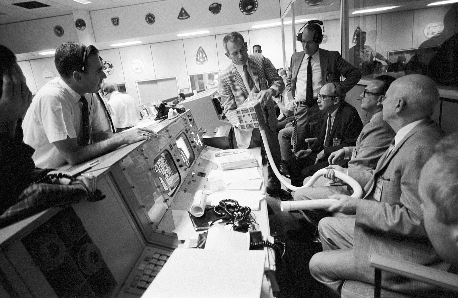 Deke Slayton mostra um adaptador de filtros a um grupo de responsáveis da NASA na sala de controle.