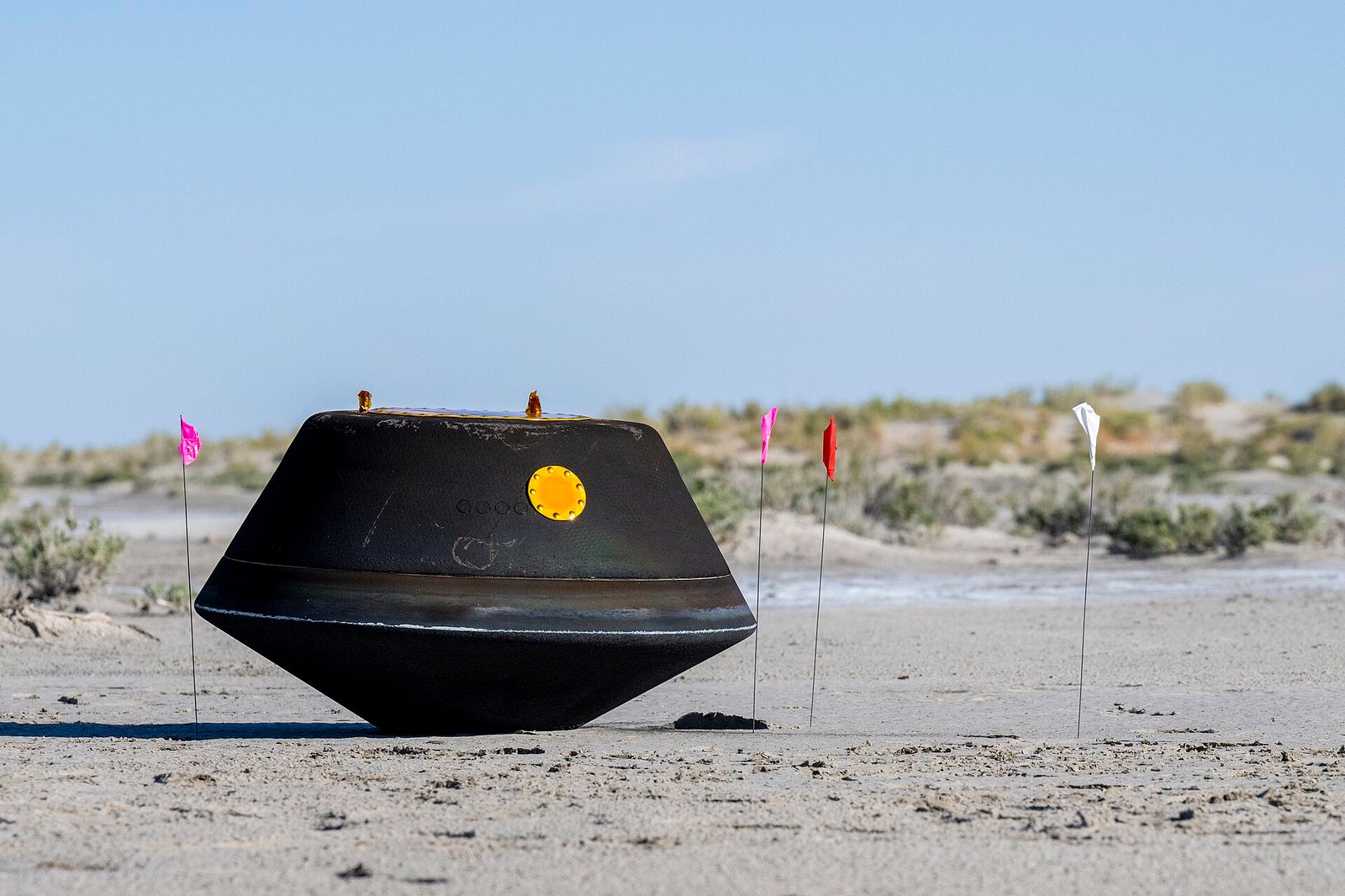 Cápsula escurecida da OSIRIS-REx repousa no solo claro do deserto após voltar à Terra.