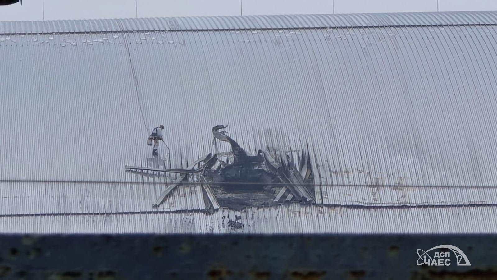 Abertura com bordas de revestimento metálico deformadas e escurecidas no arco de Chernobyl, em fotografia com a marca ChNPP.