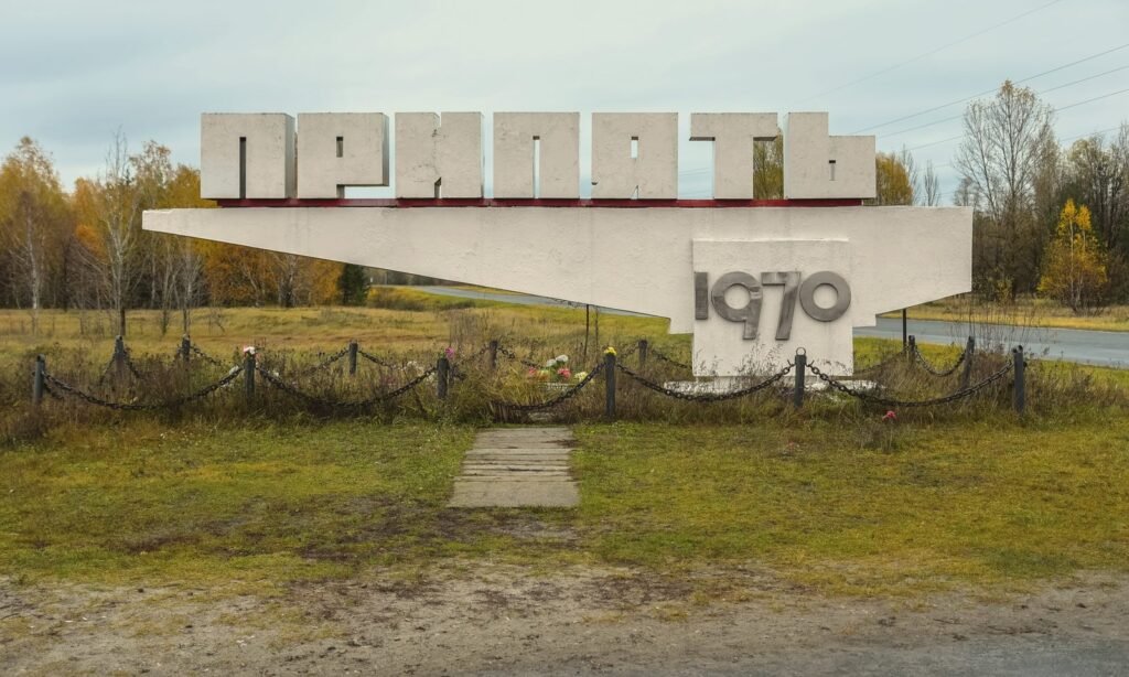 Num gramado, um monumento de concreto branco com letras grandes do alfabeto cirílico e, embaixo, o número 1970; ao fundo, árvores de outono.