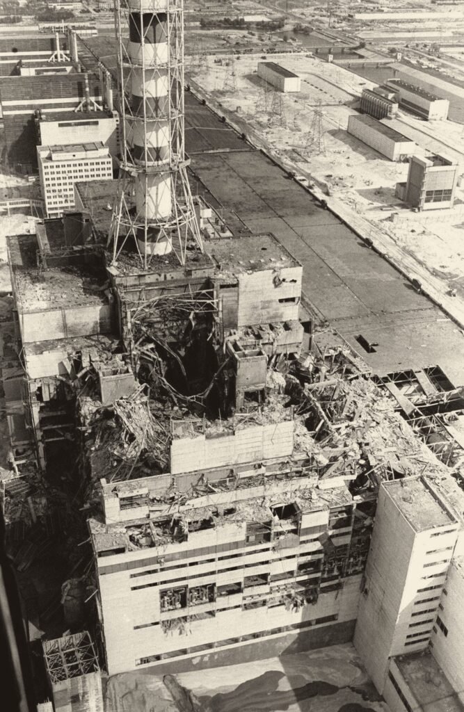 Foto aérea: um conjunto de prédios industriais; no centro, um deles está arrebentado, com um buraco escuro no lugar do teto; ao lado, uma chaminé alta com armação.