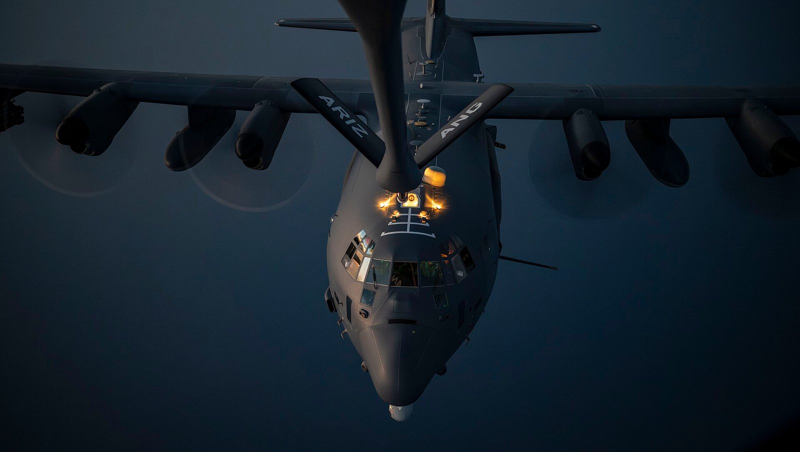 Um avião militar cinza de quatro hélices voa abaixo da aeronave de reabastecimento.