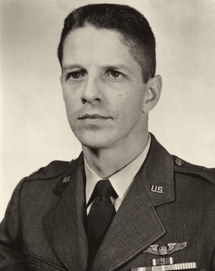 Retrato em preto e branco de um homem de cabelo curto, de farda, com um brevê de piloto no peito.
