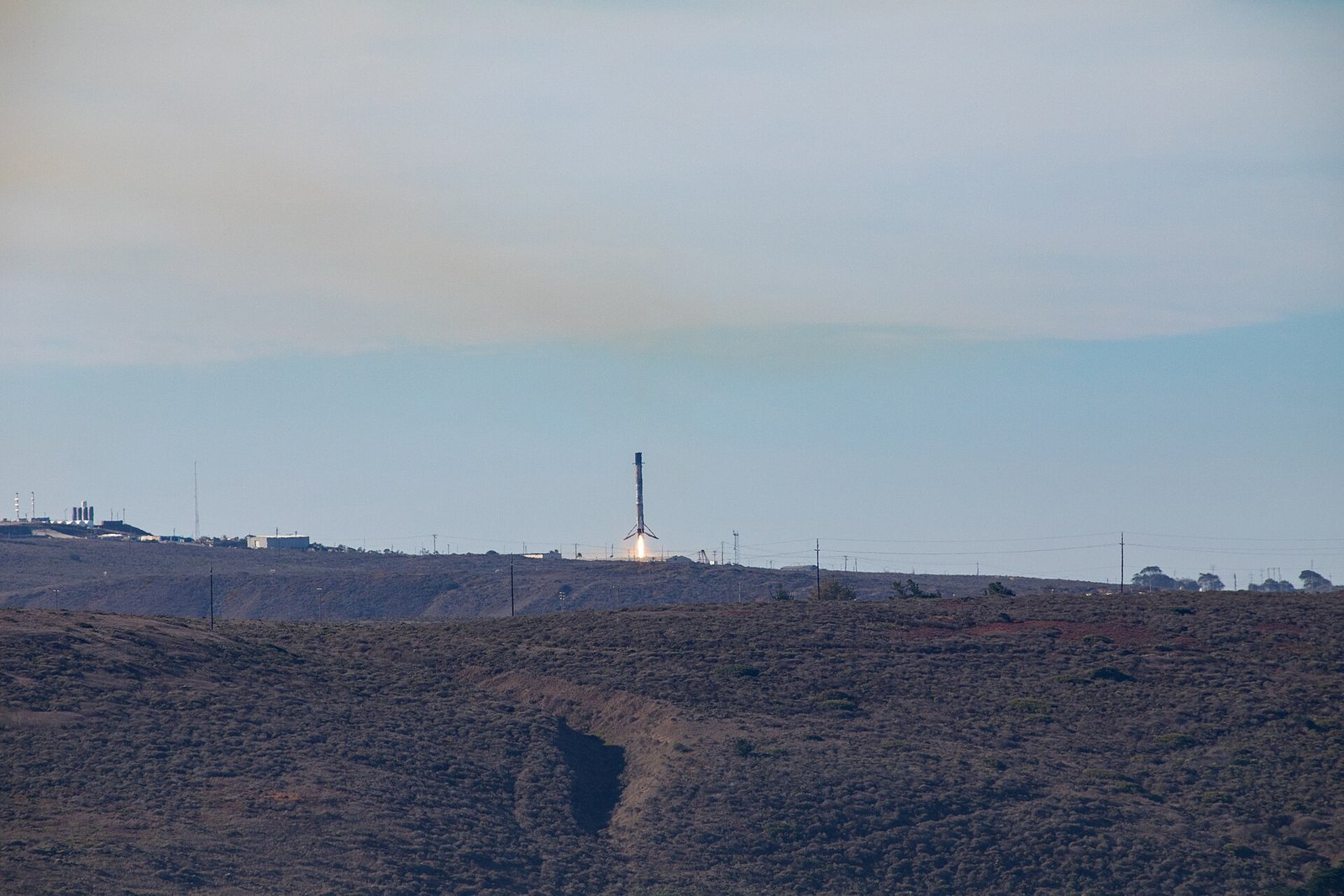 Primeiro estágio do Falcon 9 desce verticalmente, com chamas saindo da base, sobre a área de pouso.