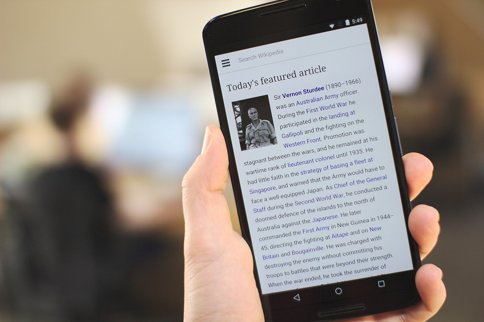 Mão segurando um telefone Nexus 6 com a página da Wikipédia aberta, num escritório.