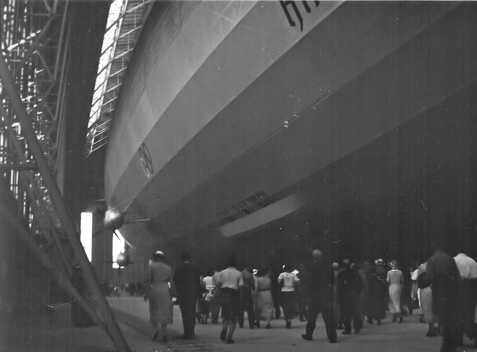 O Hindenburg ocupa um grande hangar em Frankfurt, com os anéis olímpicos próximos da frente e pessoas no chão.