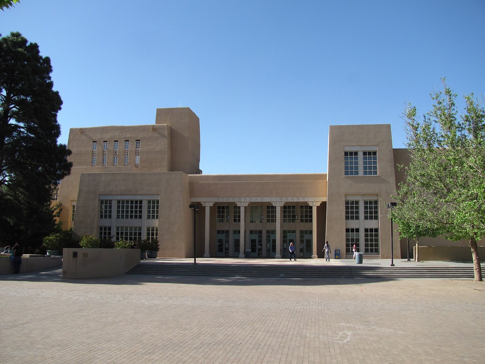 Fachada em estilo arquitetônico do sudoeste americano da Biblioteca Zimmerman, na Universidade do Novo México, com árvores e céu azul.