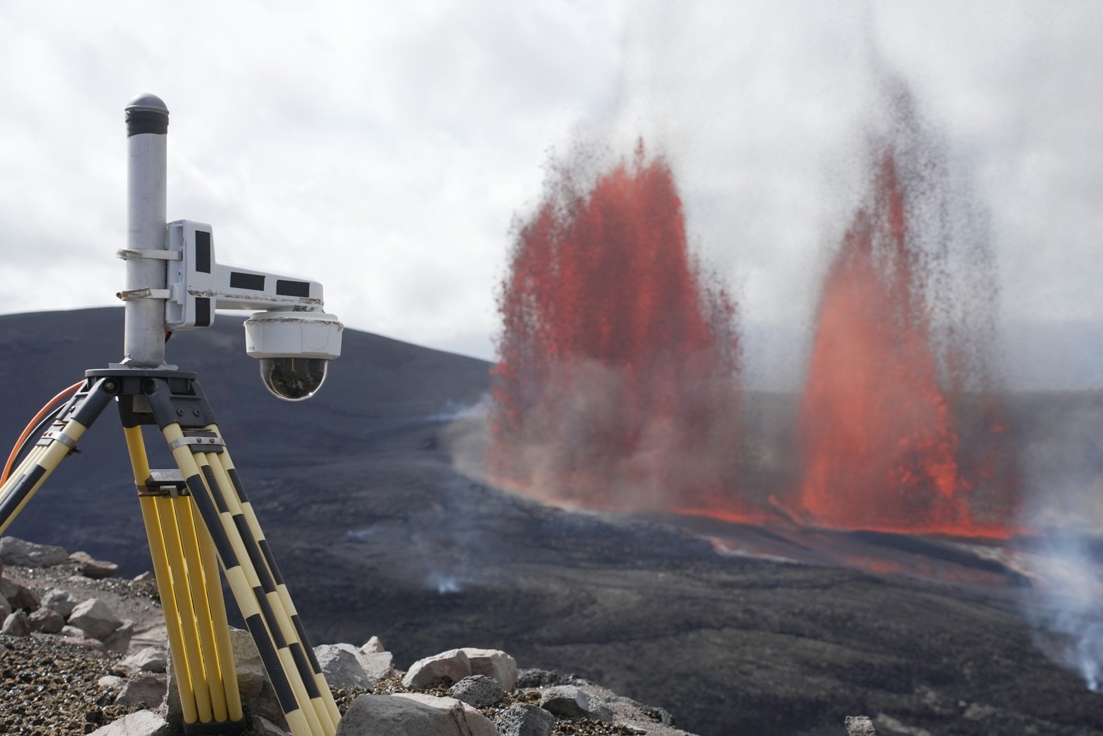 Fontes de lava alaranjadas sobem dentro da cratera, atrás de uma câmera instalada na borda.