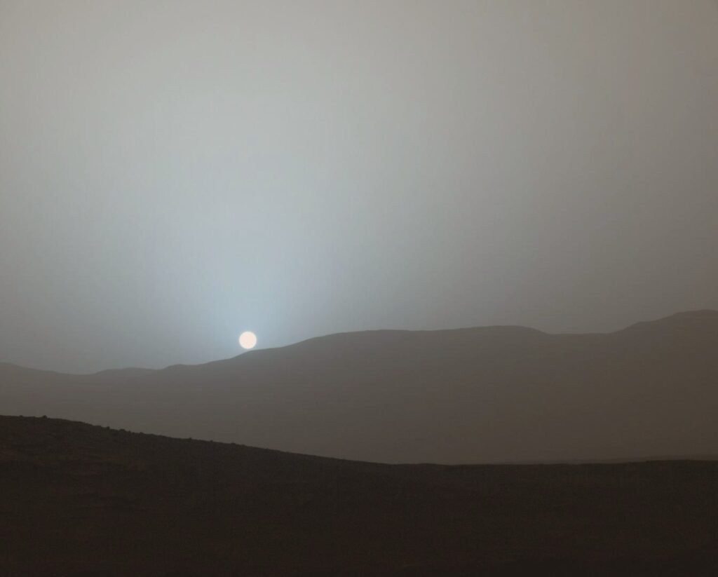 Pôr do sol em Marte: o Sol pequeno perto do horizonte, cercado por um brilho azulado.