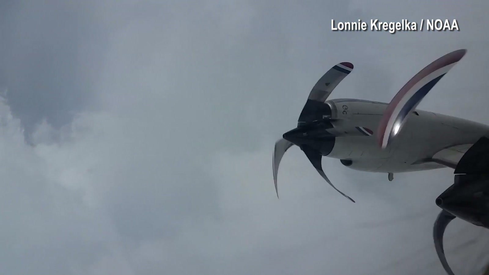 Uma hélice do avião aparece diante de uma camada espessa de nuvens claras.
