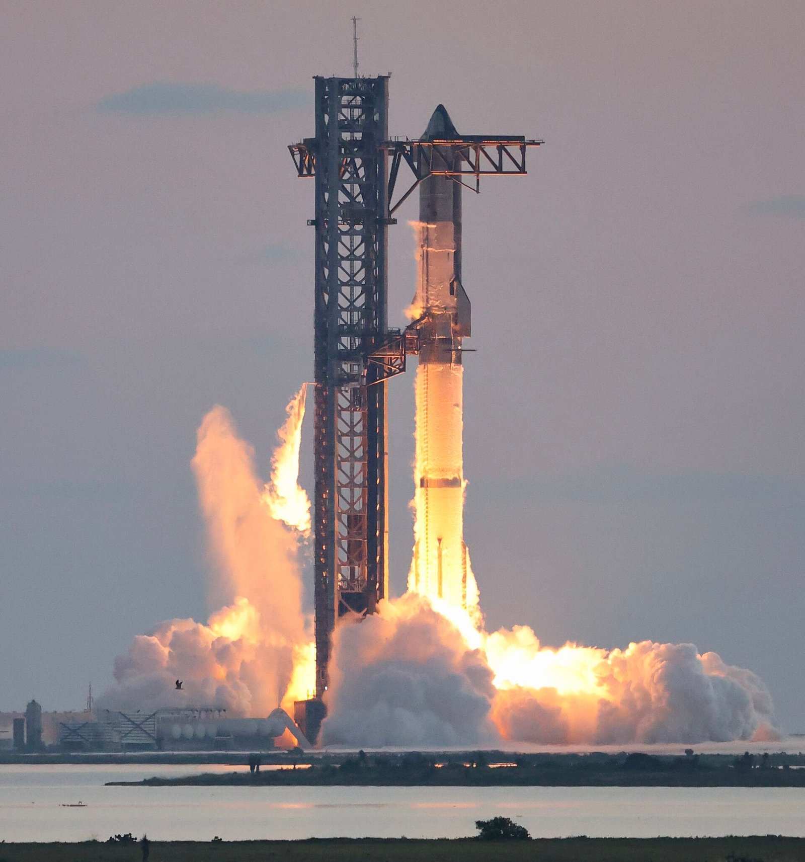 Starship e Super Heavy na torre de lançamento, com chamas e uma grande nuvem de fumaça na base.