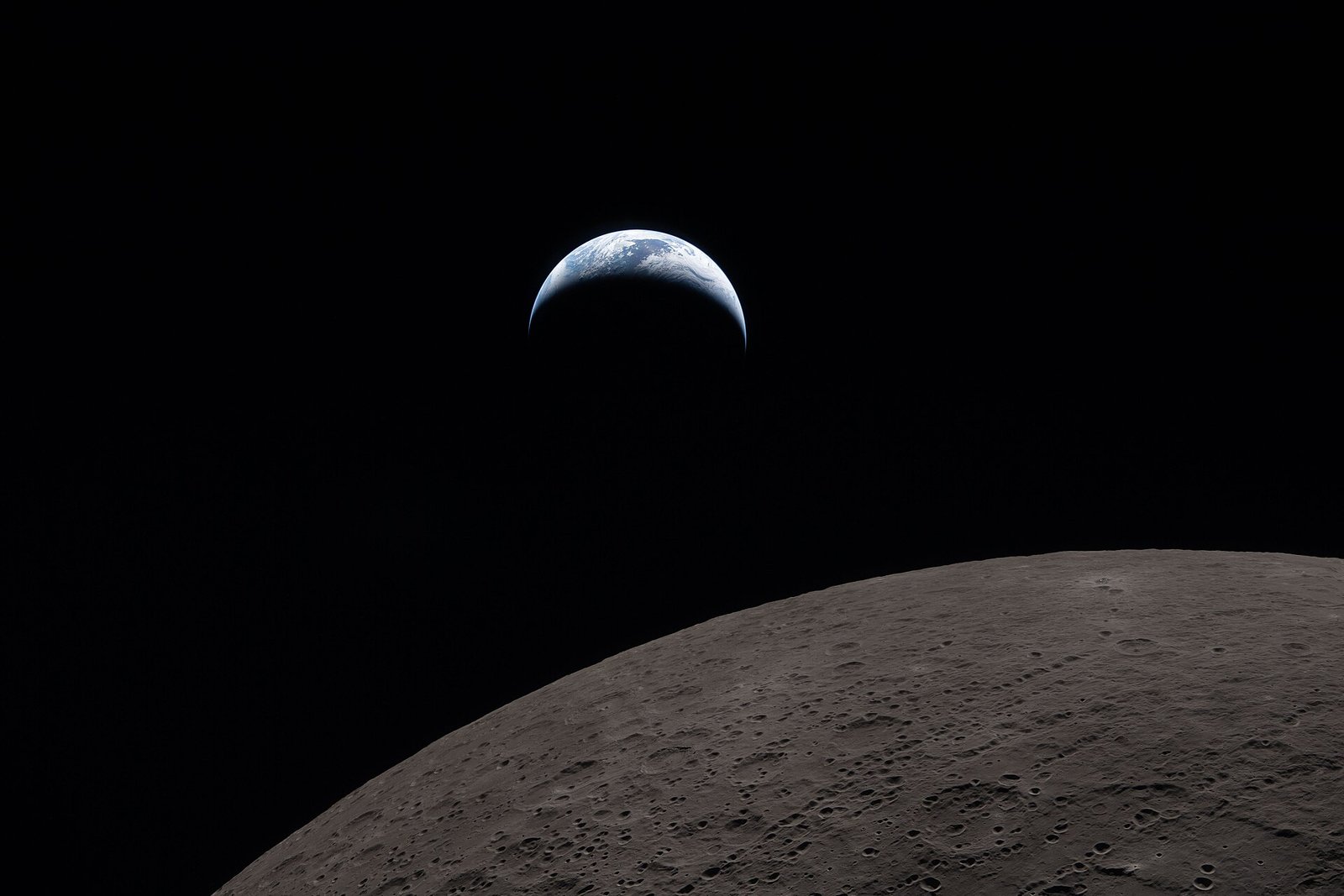 Terra com nuvens claras e uma faixa azul paira acima do horizonte escuro da Lua, em fotografia feita da Orion.