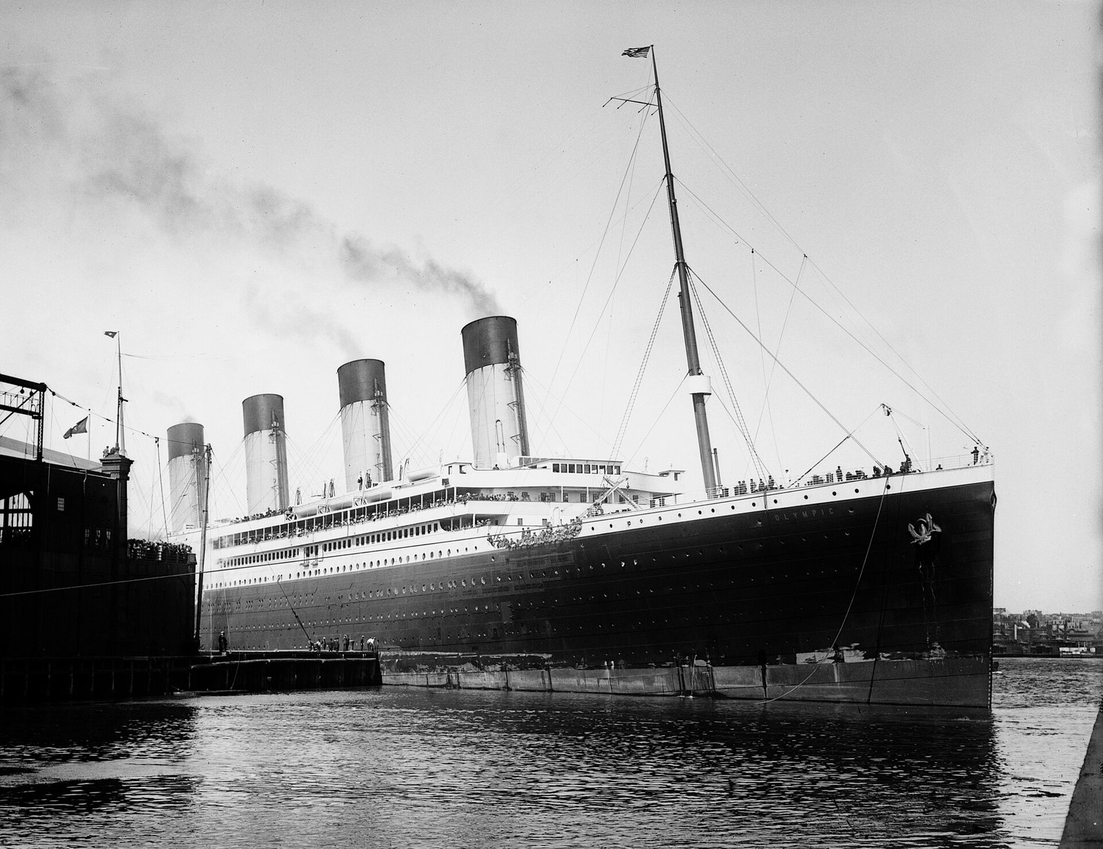 O Olympic fotografado de frente no porto de Nova York, com quatro chaminés e embarcações menores próximas.