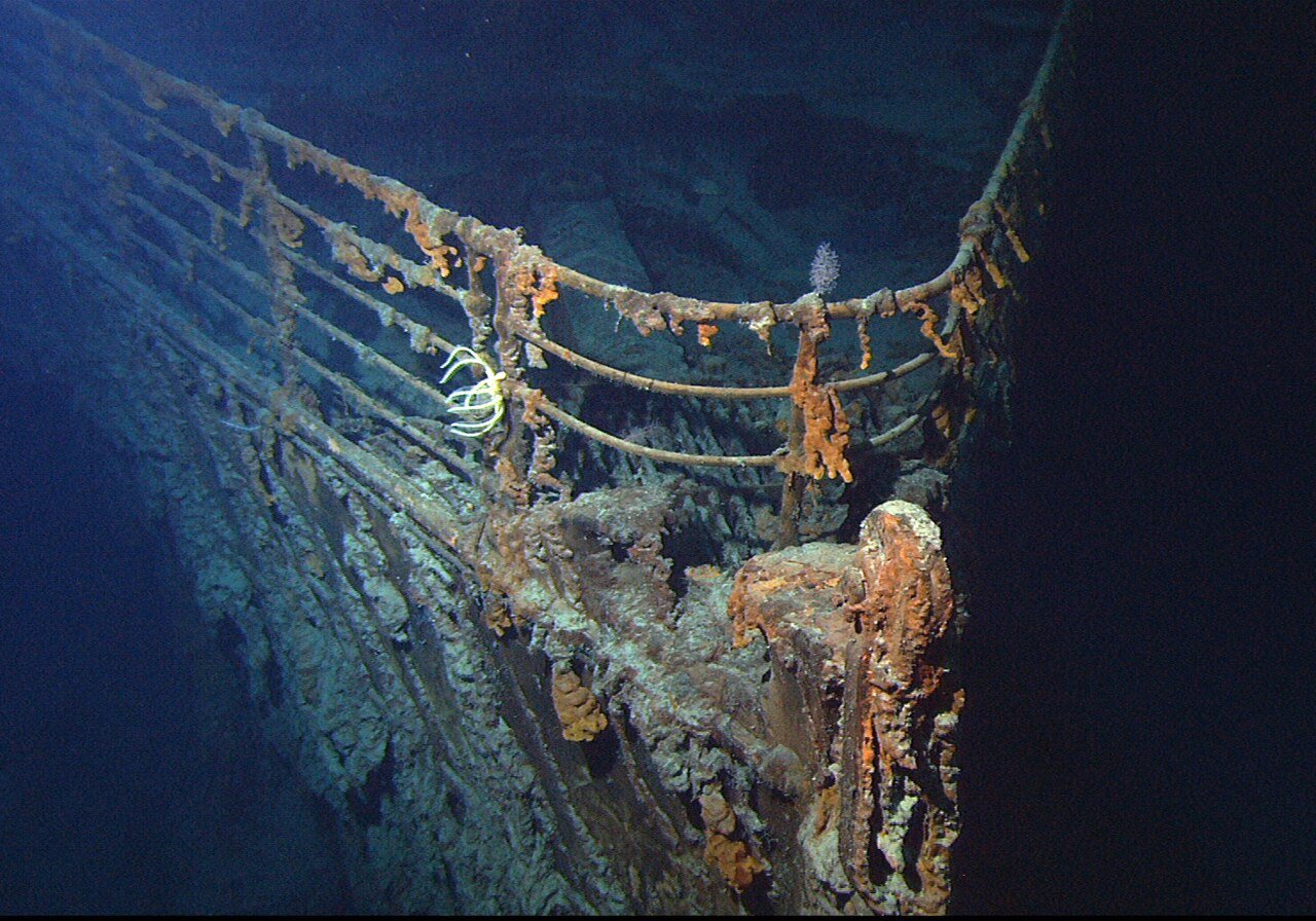 Proa corroída do Titanic sobre o leito marinho, iluminada pela câmera de um veículo submarino.