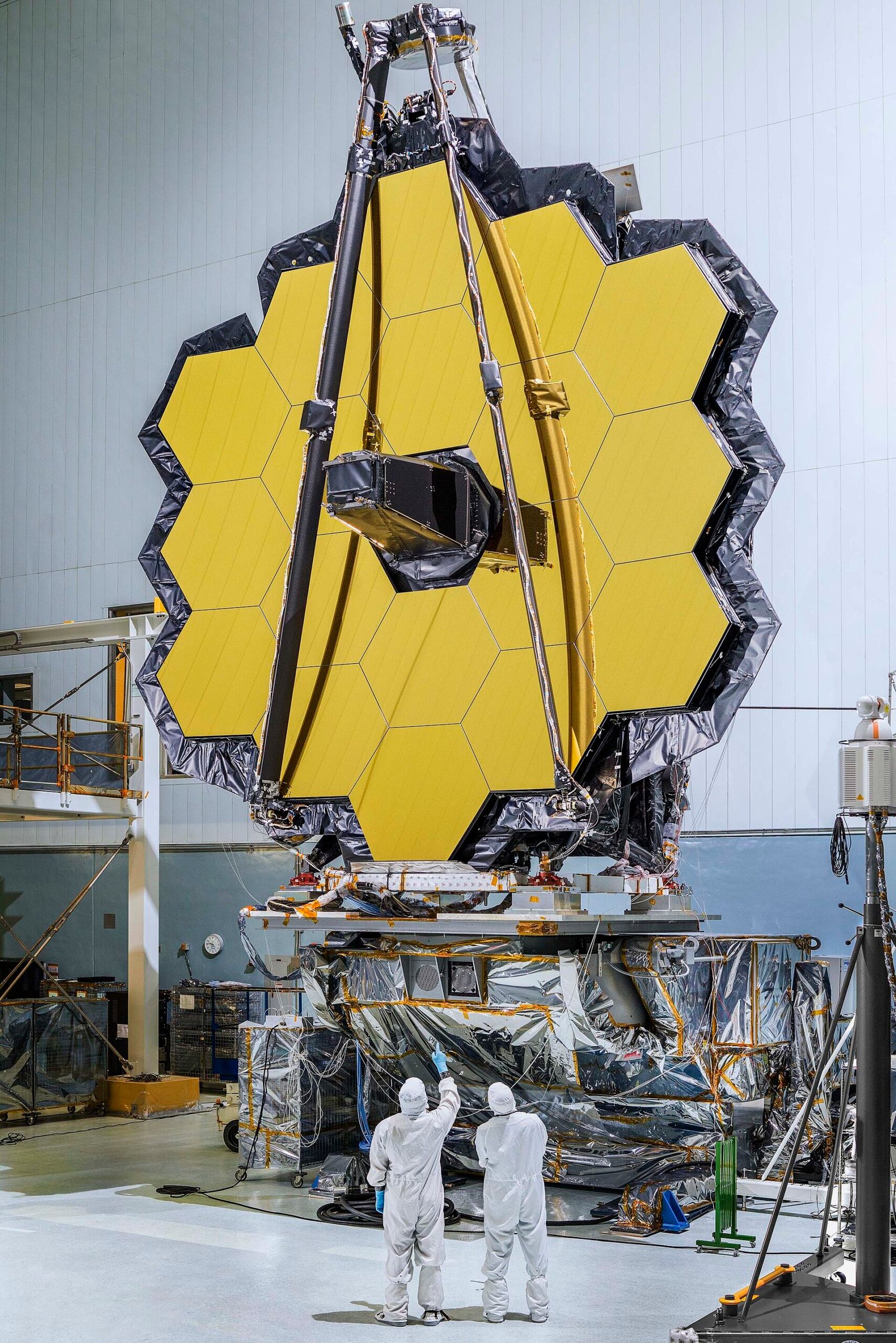 O conjunto de espelhos hexagonais dourados do Webb está montado verticalmente num suporte, dentro de uma grande sala de integração.